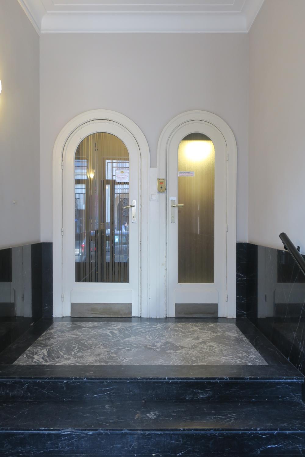 Rue de Savoie 95. Ascenseur au rez-de-chaussée (à droite) et porte d'accès vers l'escalier © Homegrade, 2023